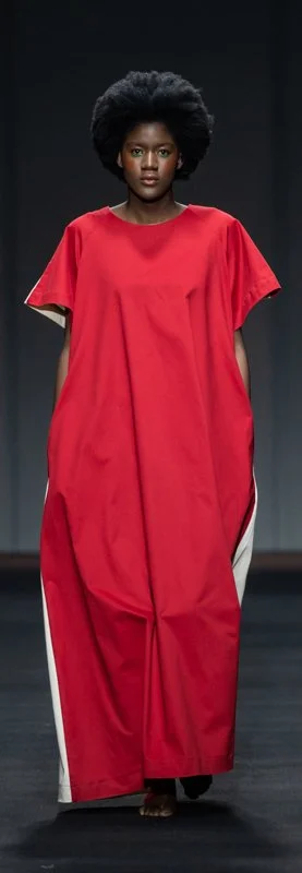 Model wearing a loose red dress with white side panels on a runway.
