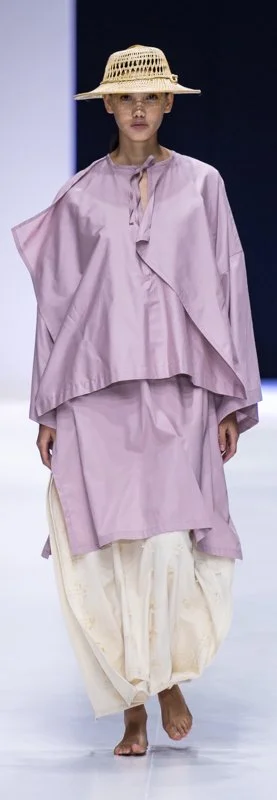 Model on runway in oversized lavender top, cream skirt, straw hat