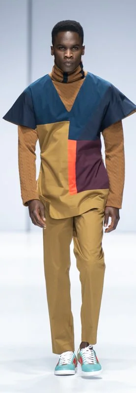 Male model wearing a geometric-patterned outfit with a turtleneck and colorful sneakers on a runway.