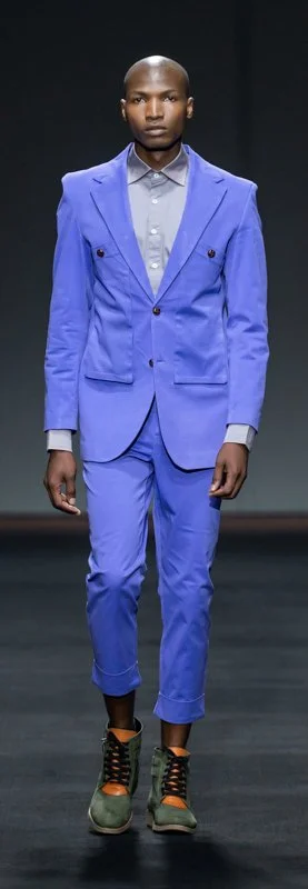 Model wearing a blue suit with cropped pants, gray shirt, and black and orange sneakers on a runway.