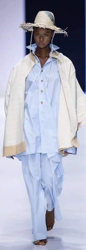 Fashion model on runway wearing oversized light blue outfit and straw hat
