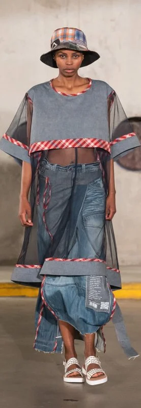Model on runway wearing avant-garde denim outfit with patchwork details and a matching bucket hat.