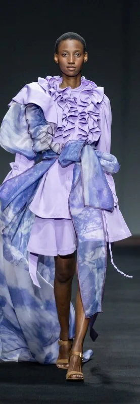 Fashion model wearing a purple ruffled dress with blue and purple sheer fabric detailing on the runway.