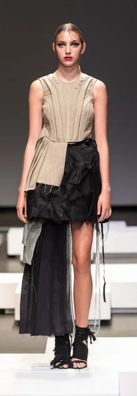 Model wearing a beige and black asymmetrical dress with layered textures on a runway.