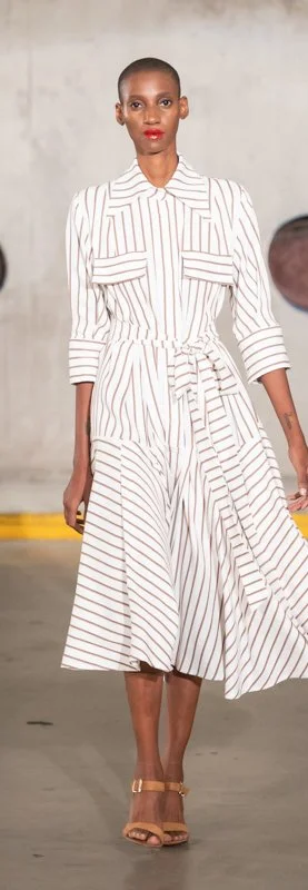 Fashion model wearing a striped dress and sandals on a runway.