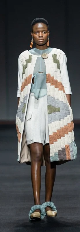 Model on runway wearing patterned coat, matching shorts, and slippers.
