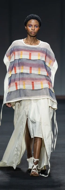 Fashion model walking on runway in layered outfit with a colorful striped top and flowy cream skirt.