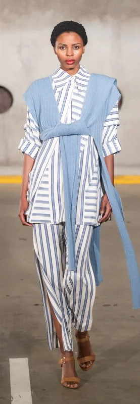 Person walking in a fashion show wearing a blue and white striped outfit with a knitted blue garment draped over the shoulders.