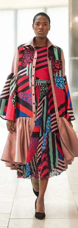 Model wearing a colorful, patterned outfit with a long, flared skirt and matching jacket in various prints.