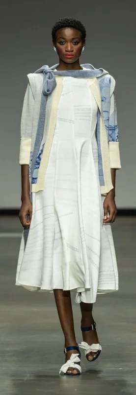 Model on runway in white dress with blue and gray scarf