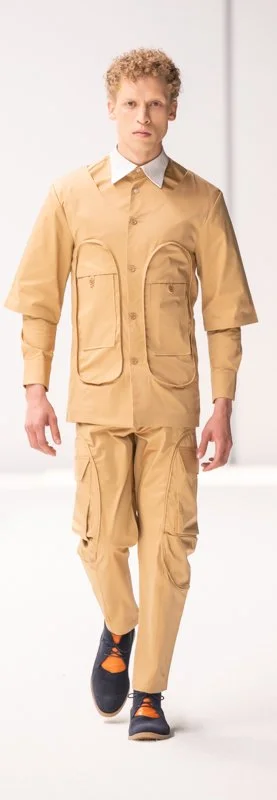 Model in tan outfit on runway, wearing shirt and pants with large pockets and dark shoes.