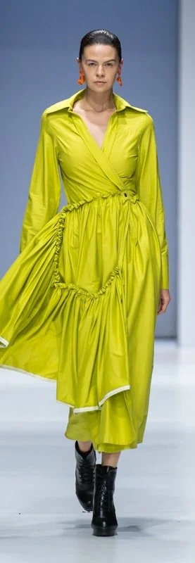 Fashion model wearing a lime green wrap dress with ruched detailing and black ankle boots on a runway.