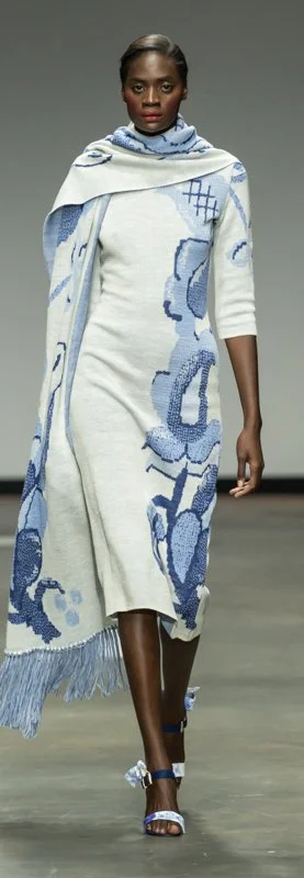 Model on runway wearing a long white and blue patterned dress with a matching scarf.