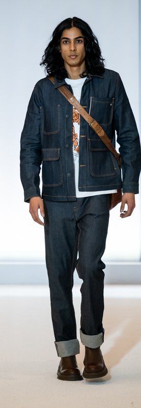 Model on runway wearing denim jacket, jeans, white T-shirt, and brown crossbody bag