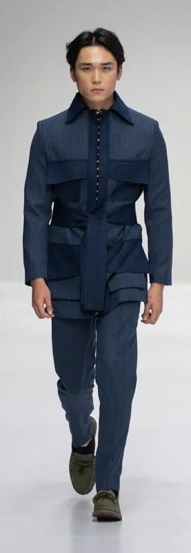 Model in a stylish blue suit with a layered design, walking on a runway.