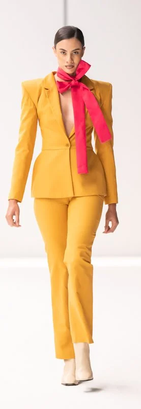 Person wearing a bright yellow tailored suit with a bold red bow tie, walking on a runway.