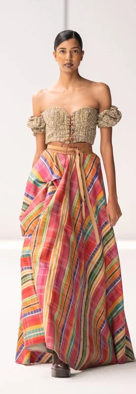 Model wearing off-the-shoulder top with a colorful striped skirt on the runway.
