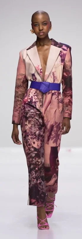 Model wearing a patterned jumpsuit with a purple belt on a fashion runway.