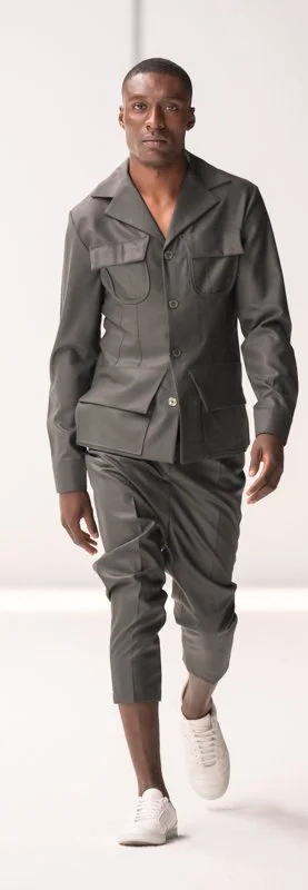 A model walking on a runway wearing a gray tailored outfit and white sneakers.