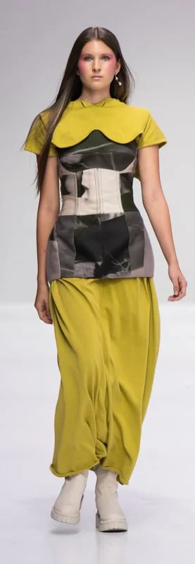 Fashion model wearing a yellow and black outfit with a corset-style top and flowy pants on a runway.
