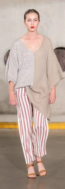 Model wearing an asymmetric knit sweater with loose striped pants on a runway.
