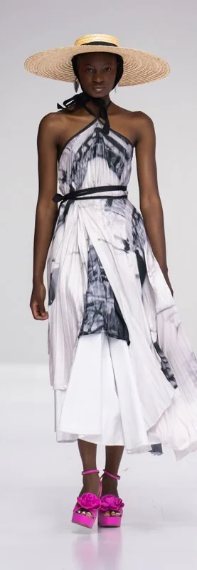 Fashion model wearing a black and white patterned dress with a wide-brimmed straw hat and bright pink platform sandals.