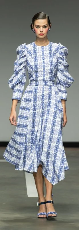 Model wearing a blue and white patterned dress with puffed sleeves on a runway.