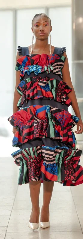Fashion model wearing a colorful ruffled dress with bold patterns and white high heels.