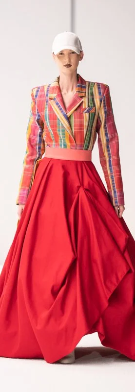 Model in colorful plaid blazer and red skirt with white cap on runway