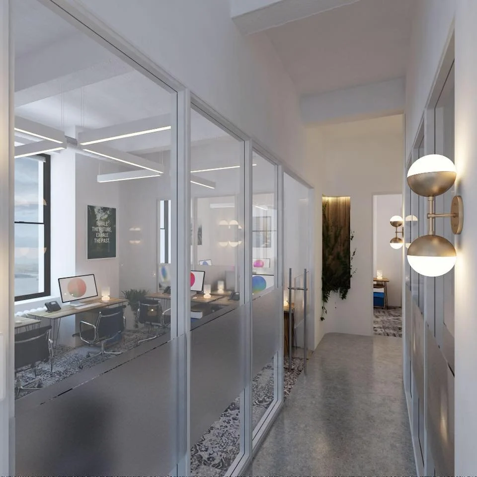 Modern office space with glass walls, desks, computers, and chairs, with natural light and contemporary wall lighting.