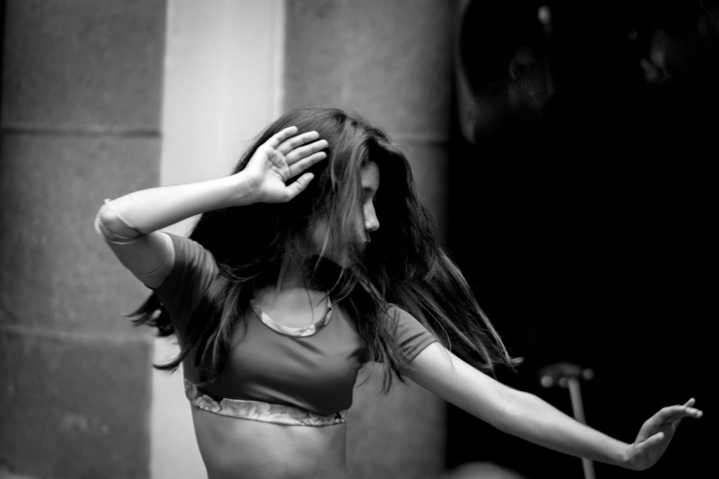 A young woman with long hair dancing with her hand raised near her head in a black and white photo.