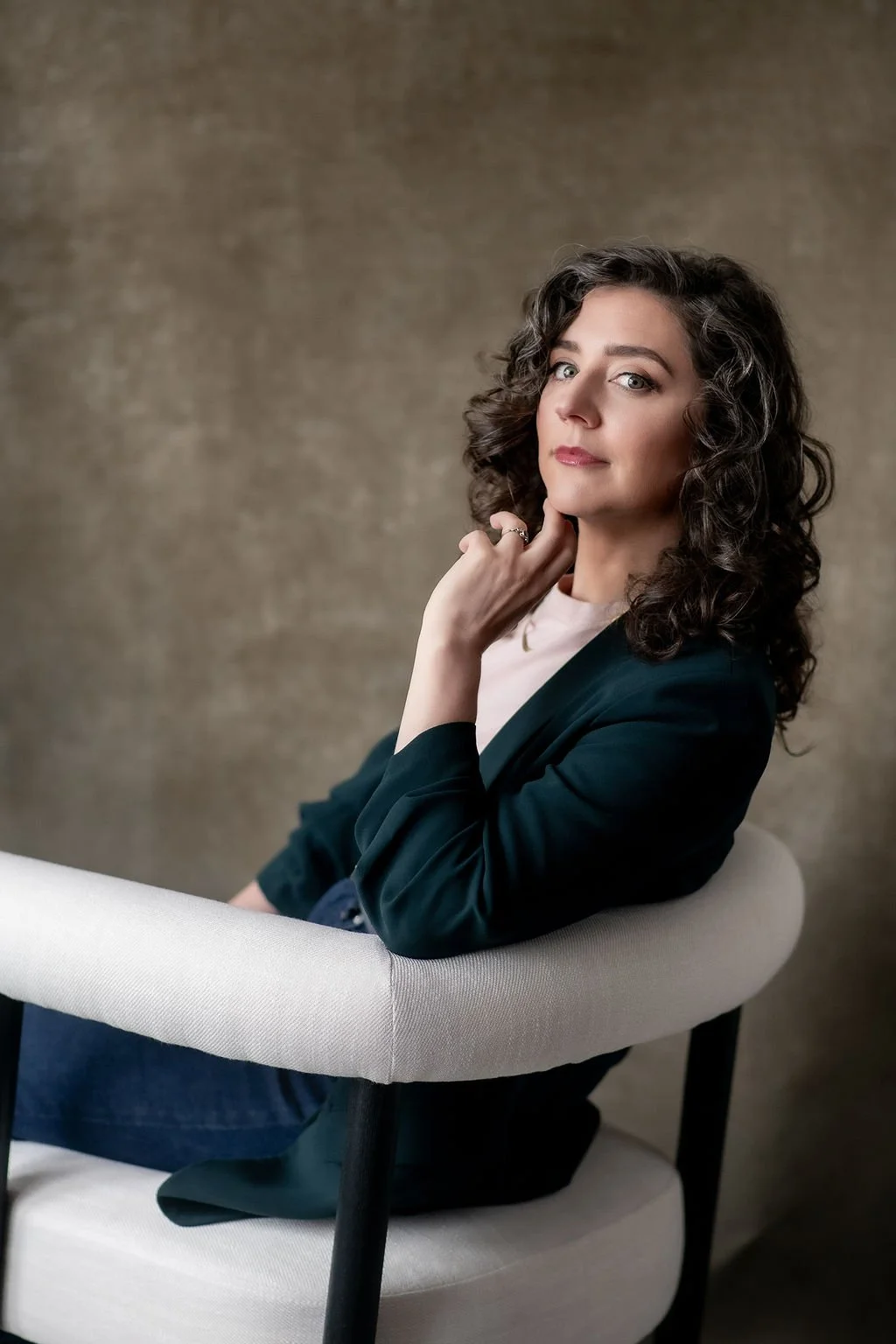 Image of Rikki Goldenberg, Career Coach, Executive Leadership Coach, sitting in a chair wearing a pink shirt and green blazer