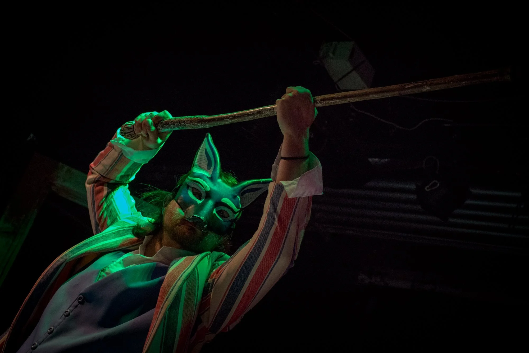 A man in a fox mask and a suit lifts a cane up menacingly.