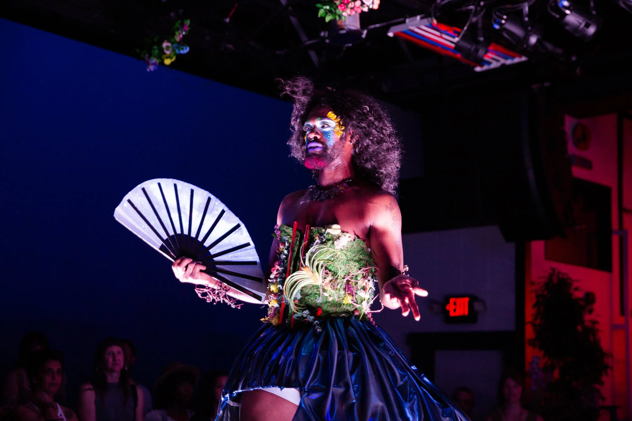 Mother Nature, dressed in a green and blue dress, struts around with a fan