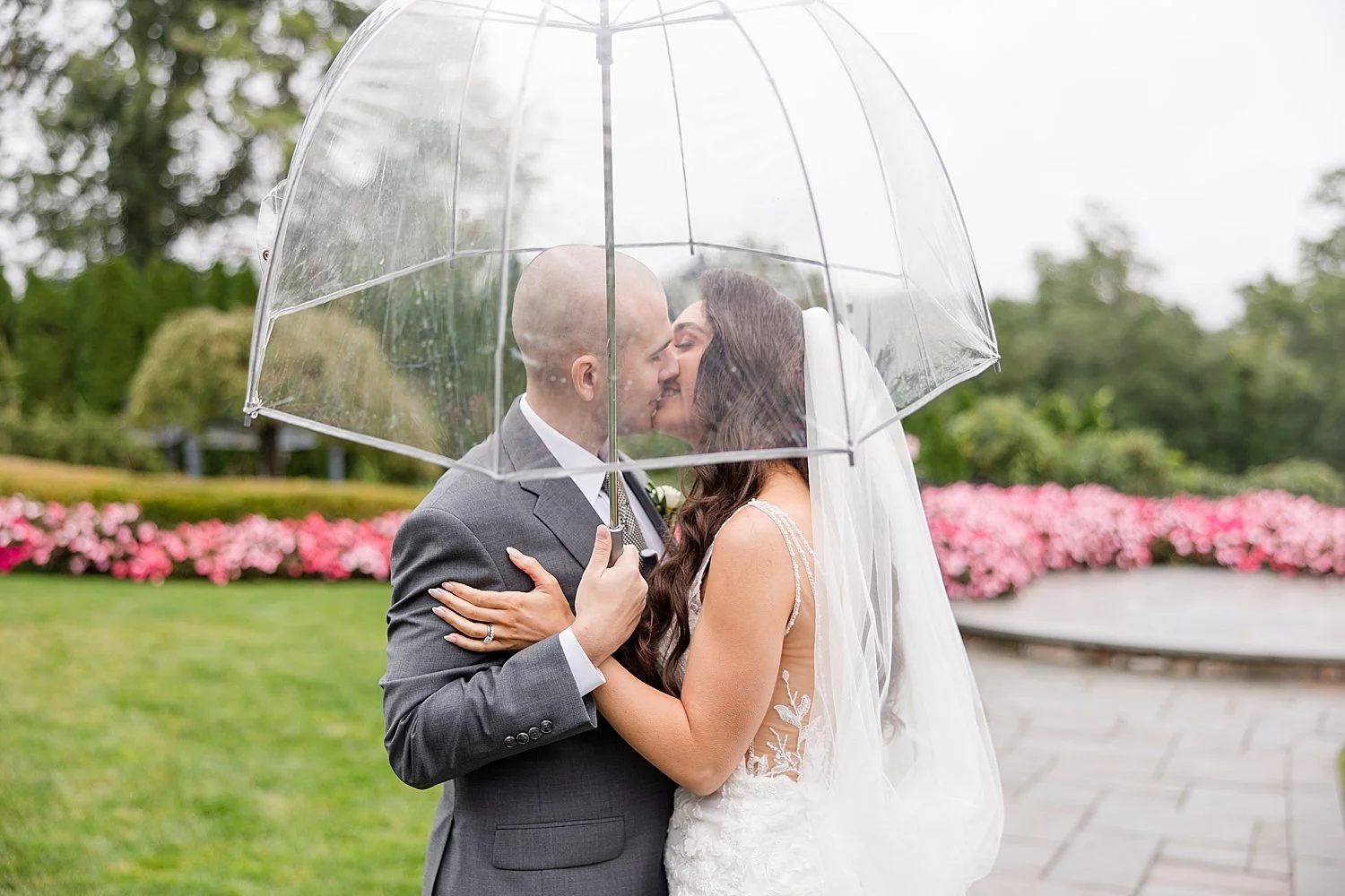  romantic rainy wedding photos of bride and groom kissing under clear umbrella  