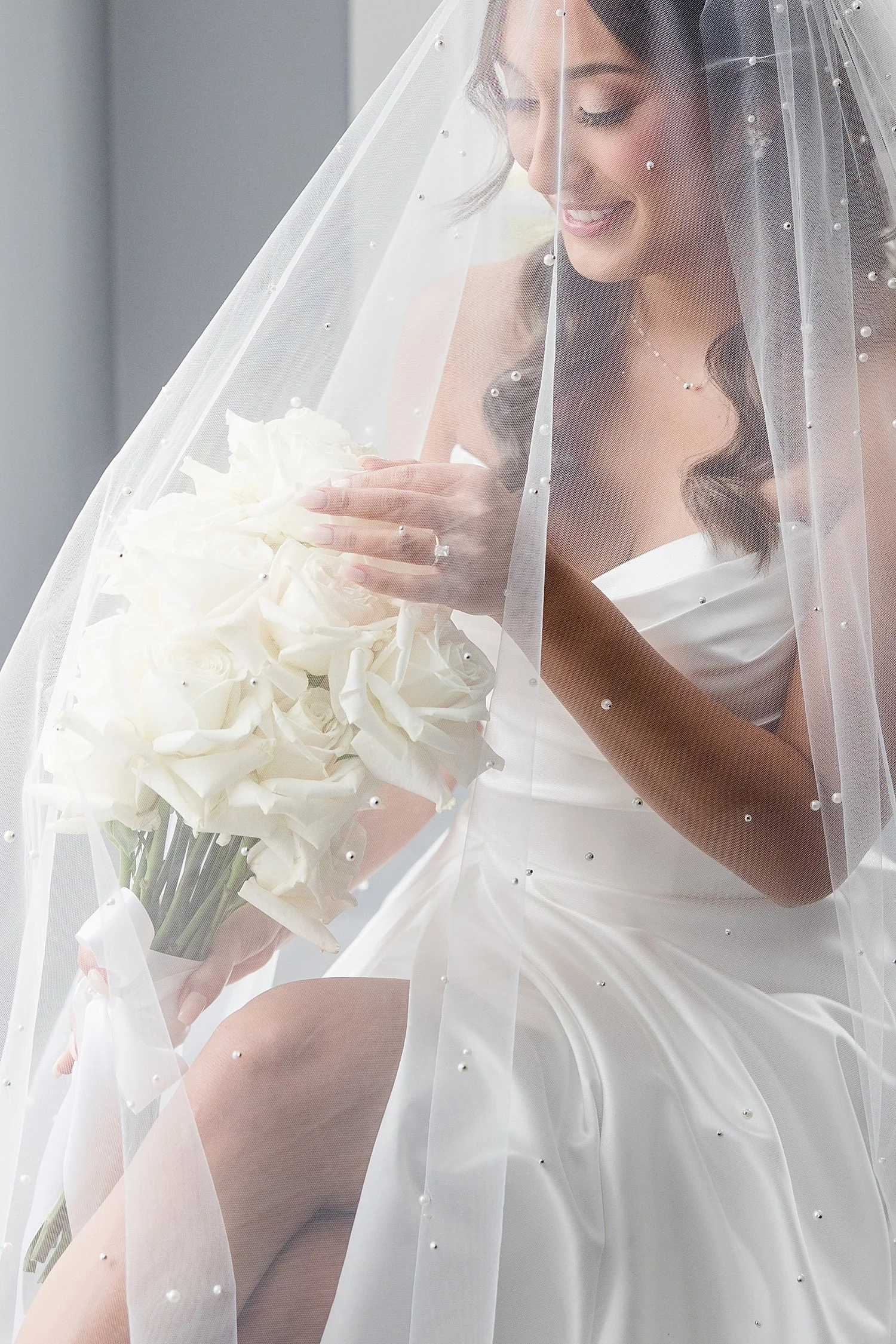  bride holding bridal bouquet under veil with pearl embellishments   