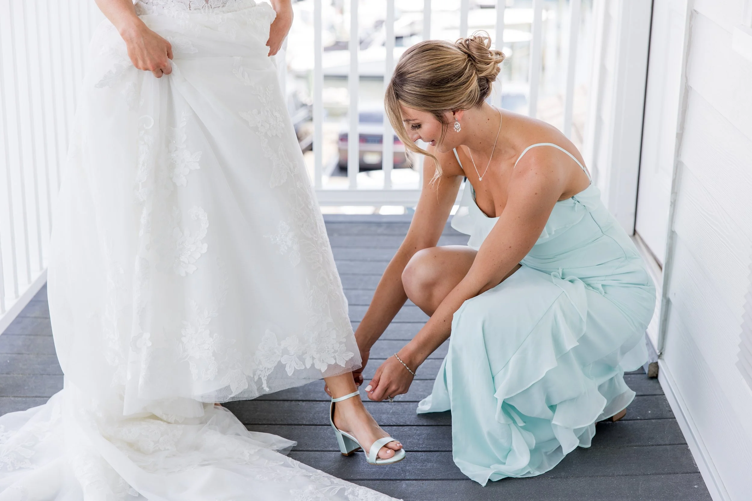 Bridesmaid helping bride buckle shoe. Getting ready photo by Jessica Anne Photography at Crystal Point Yacht Club in Point Pleasant, NJ