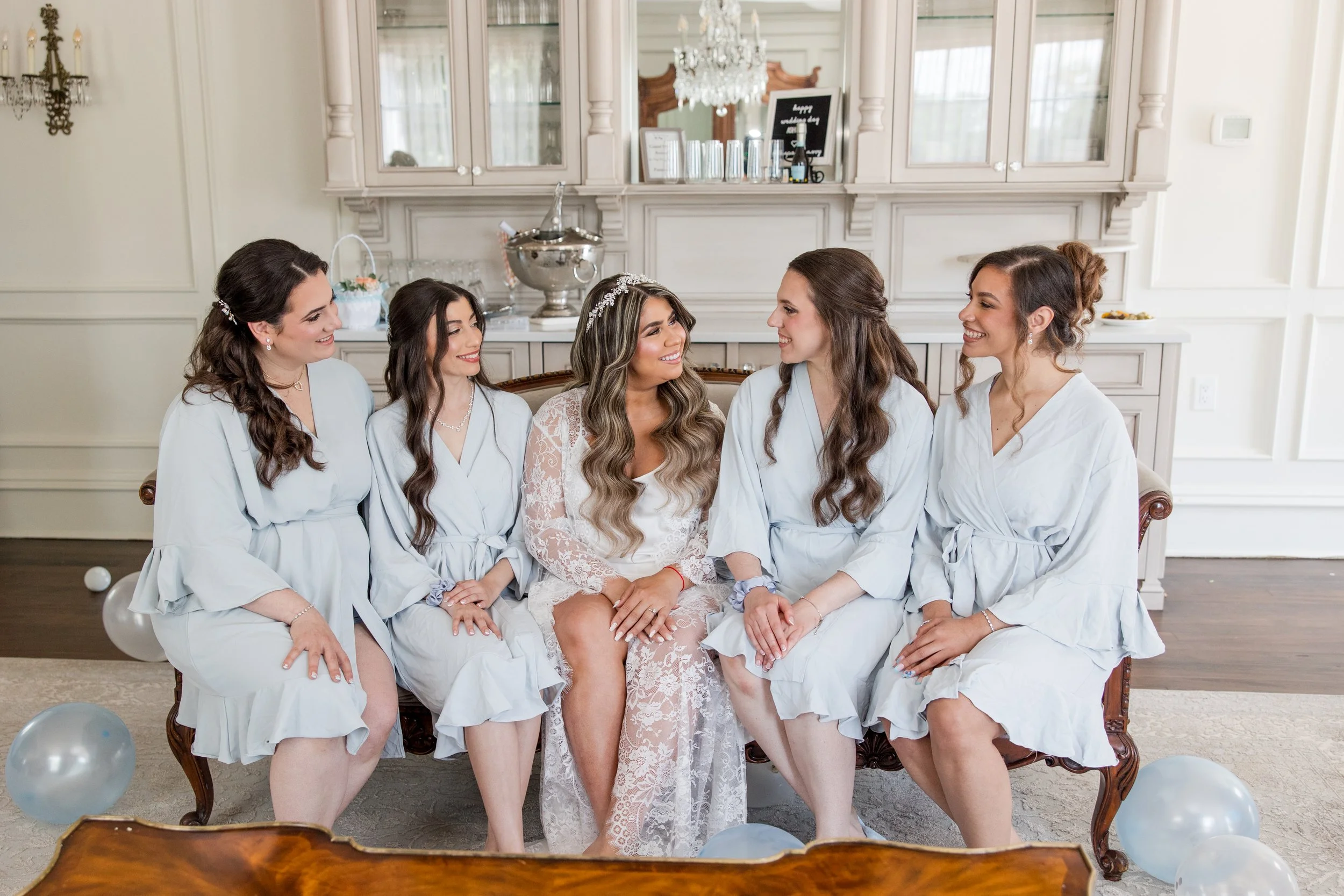 Bride and bridesmaids in matching robes sitting on couch at The Park Savoy Estate in Florham Park, NJ by wedding photographer, Jessica Anne Photography