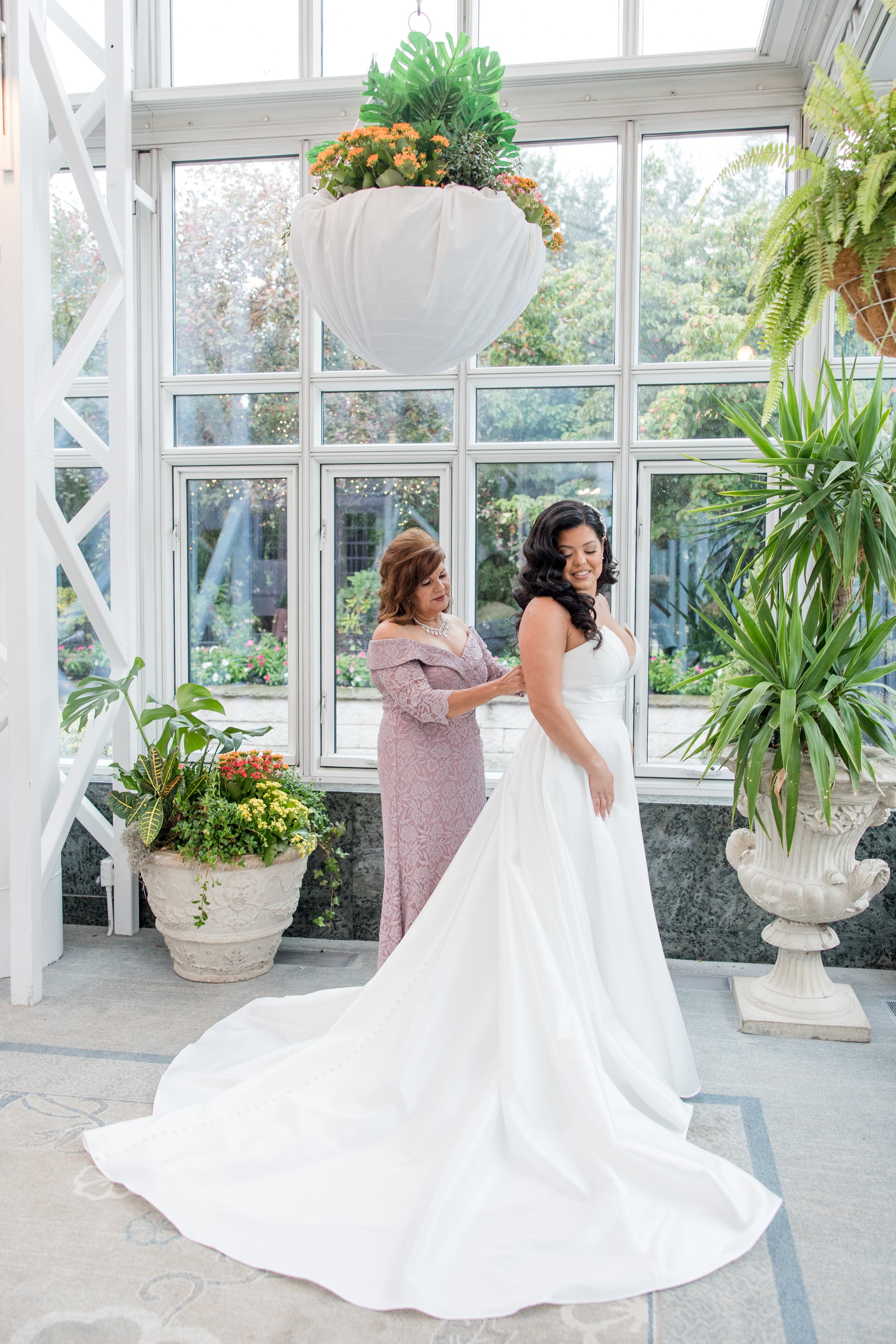 Mother of the bride fixing brides dress in greenhouse at The Park Savoy Estate in Florham Park, NJ. Shot by Jessica Anne Photography