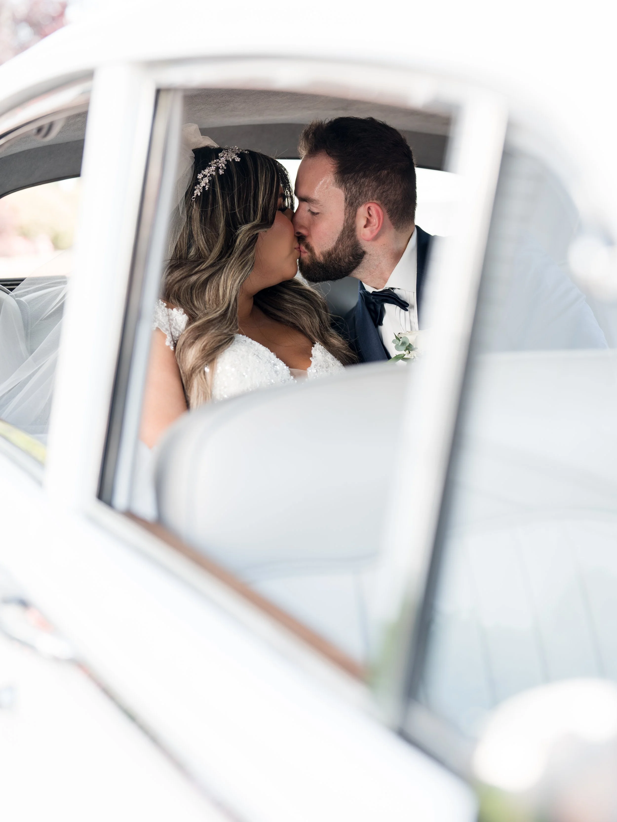 Looking through window perspective photo of bride and groom kissing in vintage car. Taken at The Park Savoy Estate in Florham Park, NJ by Jessica Anne Photography
