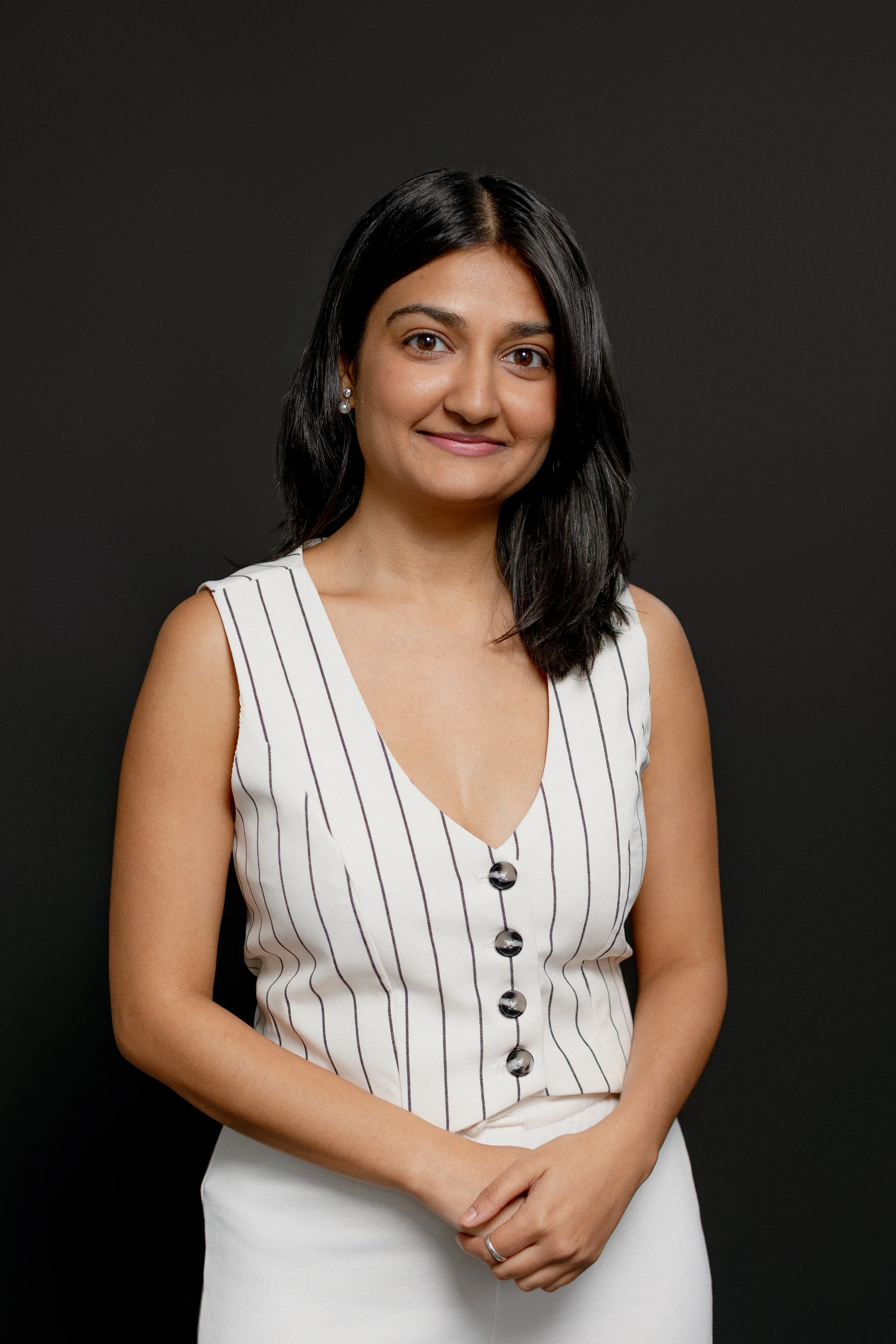 Portrait of a woman with dark hair wear a black blazer and a blue blouse against a black background.