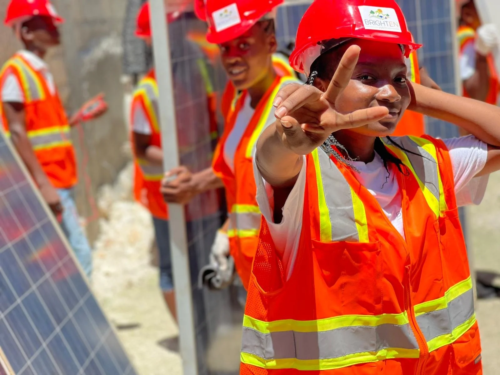 Workers wearing orange safety vests and red hard hats installing solar panels outdoors.