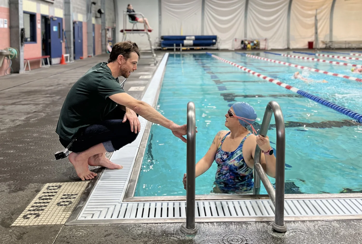 Chris Bagg crouched at the edge of the pool talking with an athlete on the steps