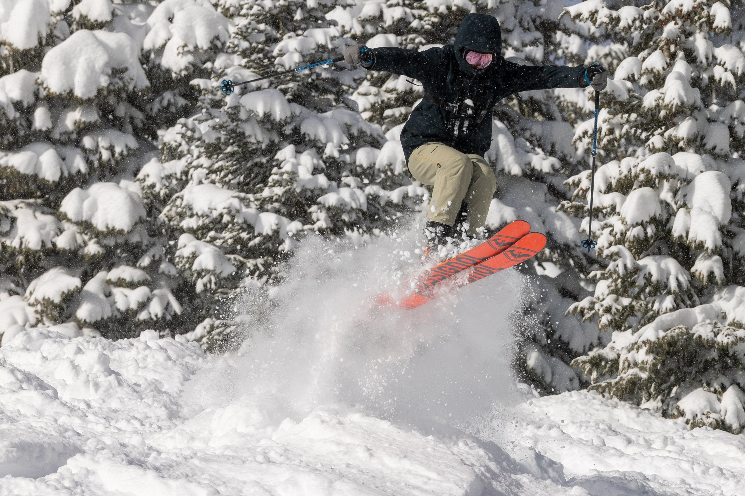 Skier in dark clothing crouches into a turn through fresh powder.