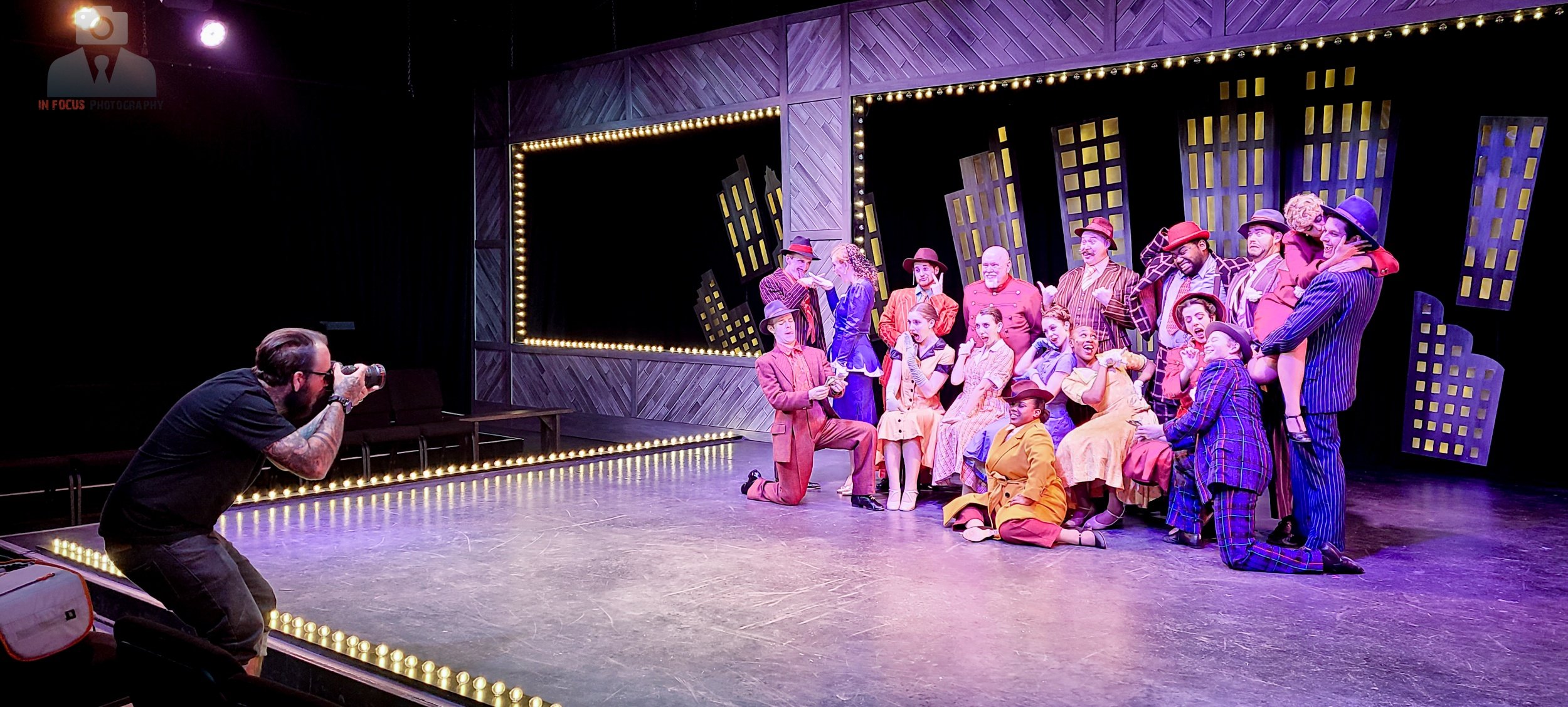 Young performers in colorful costumes dance onstage during a theater production.