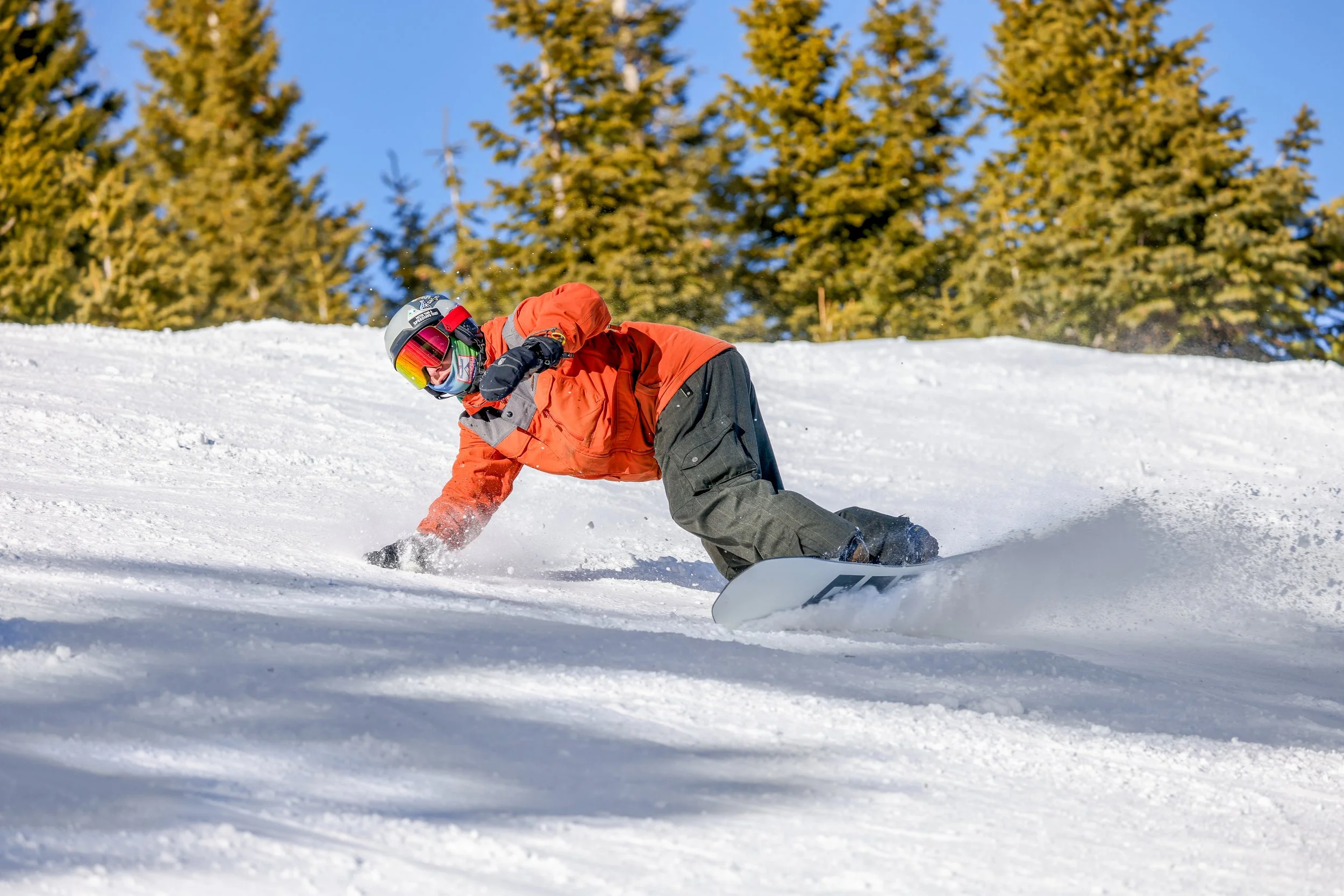 Skier in an orange jacket makes a powder turn among snow-covered trees.