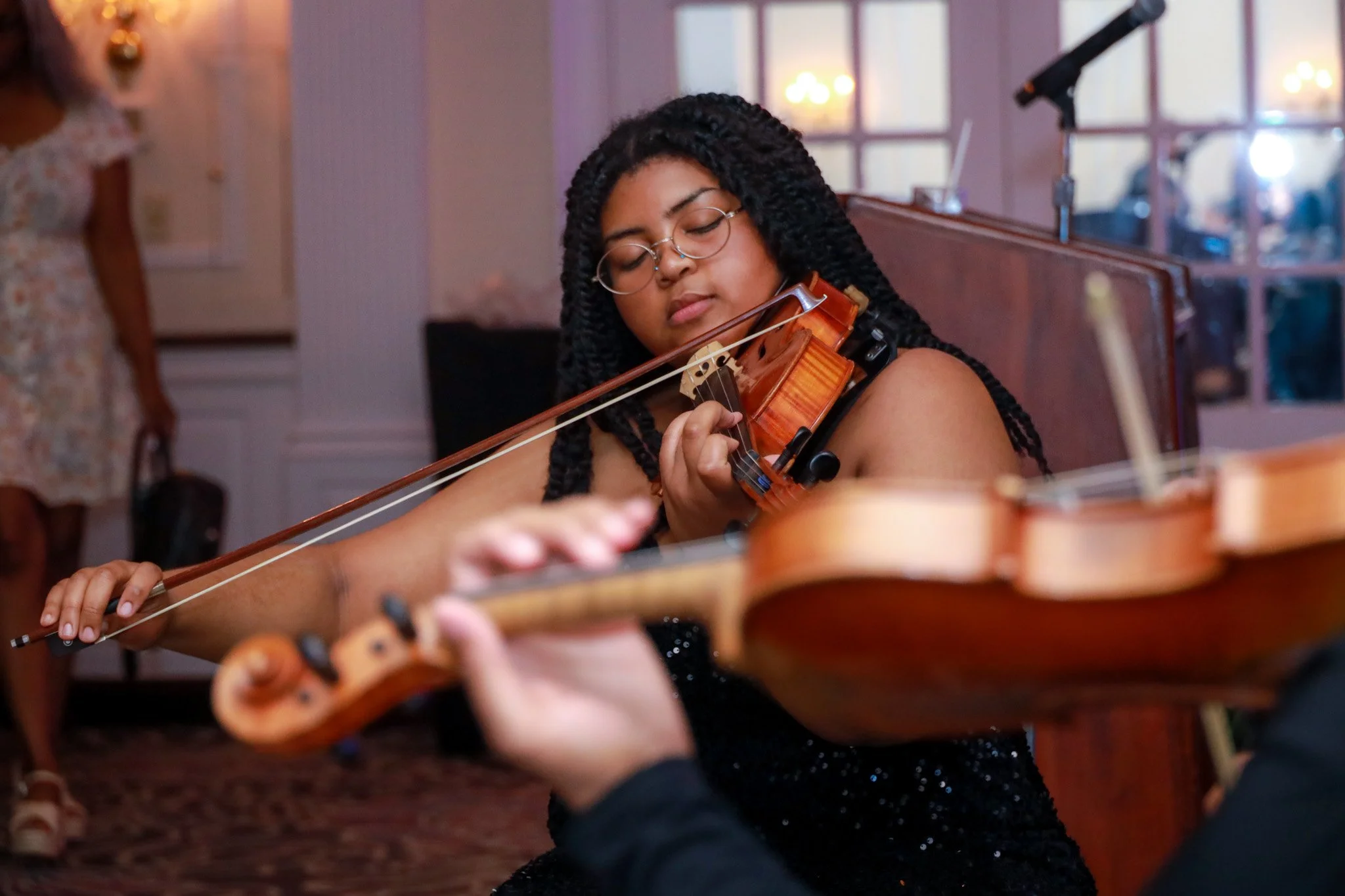 A woman with glasses and braided hair playing a violin during a performance.