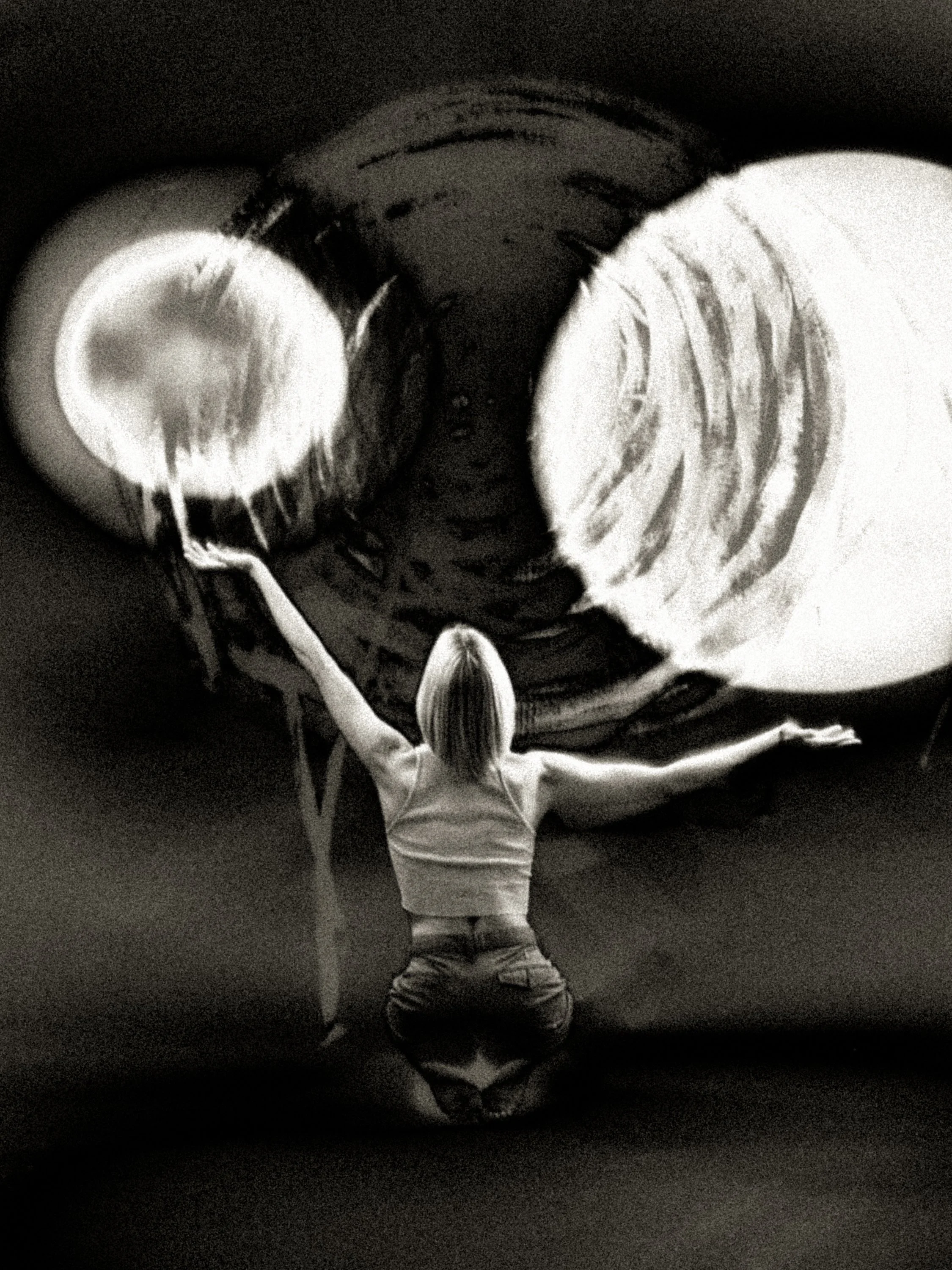 Black-and-white surreal composition of an inverted figure holding a bright orb beneath a larger eclipse-like sphere, evoking reversal, transformation, and kinetic becoming.
