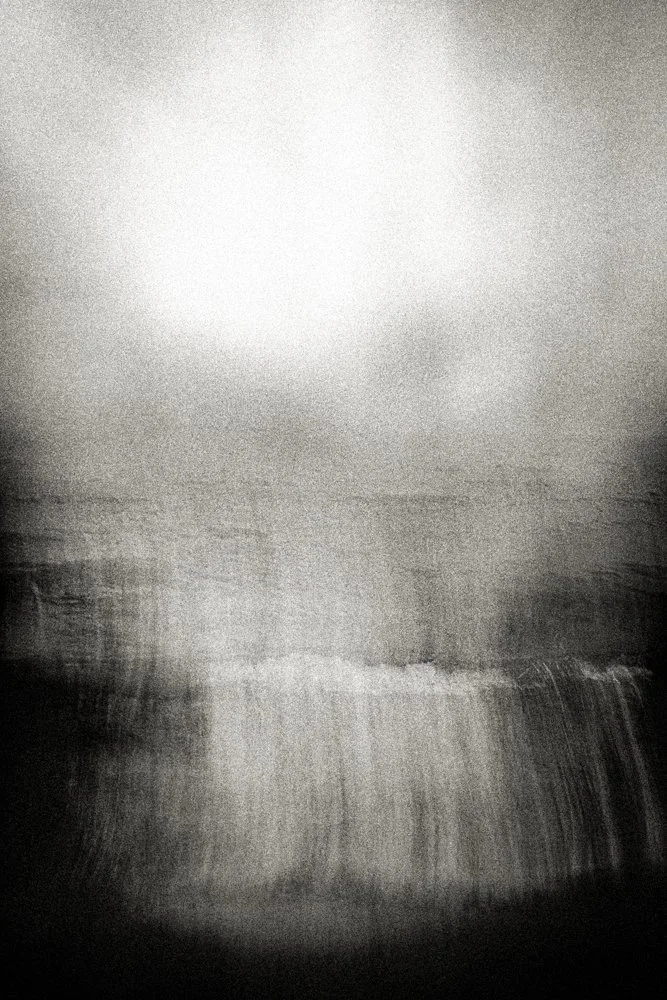 Vertical black and white seascape with radiant light breaking through clouds above a soft horizon, ethereal minimalist fine art print.