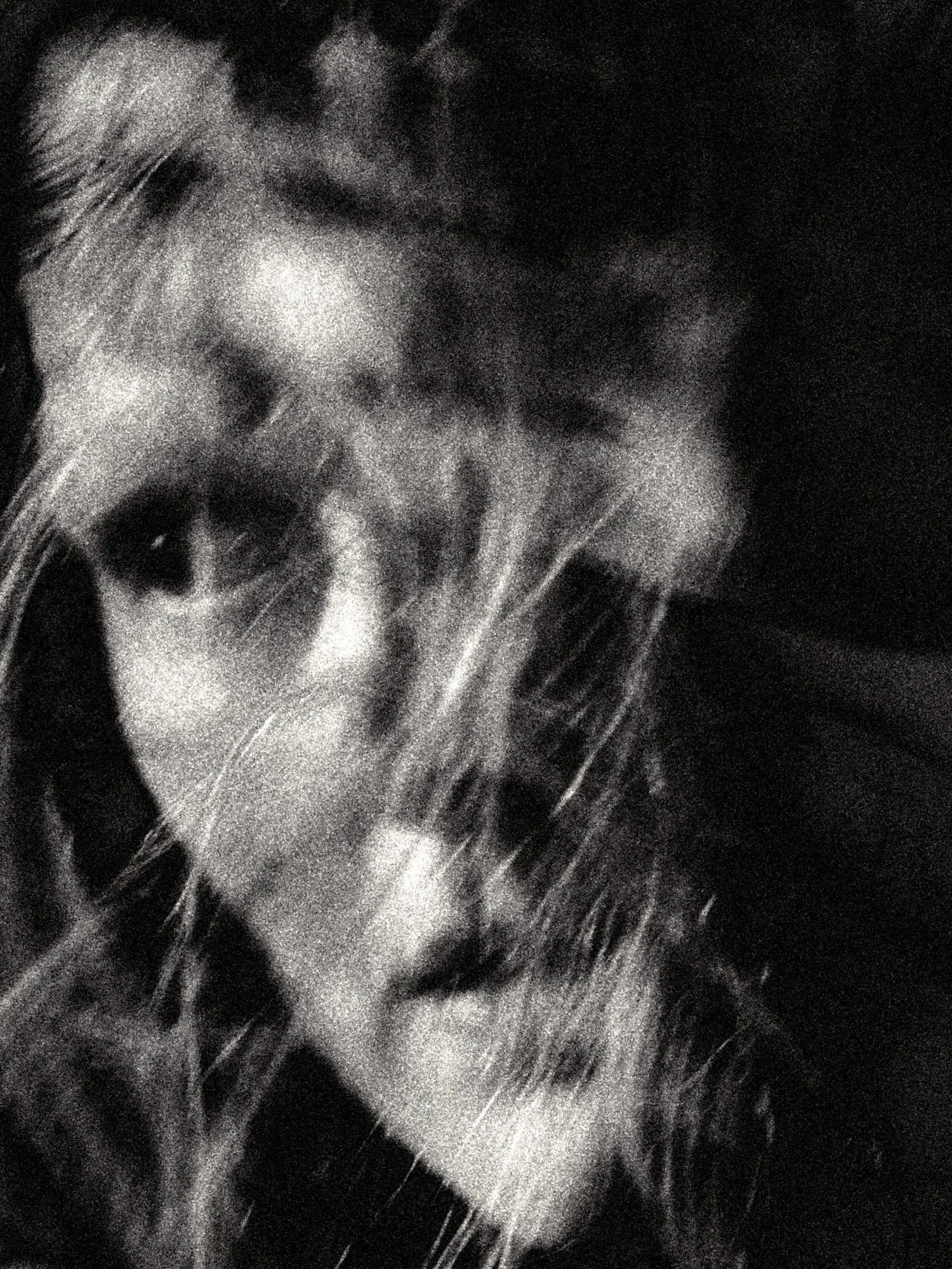 High-grain black-and-white close-up portrait with motion blur and layered facial contours, evoking masking, memory, and fragmented identity in a dark minimal frame.